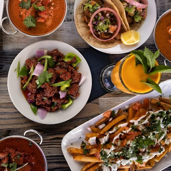Overhead view of Indian dishes: curries, tacos, chili chicken, loaded fries, and a mango lassi.