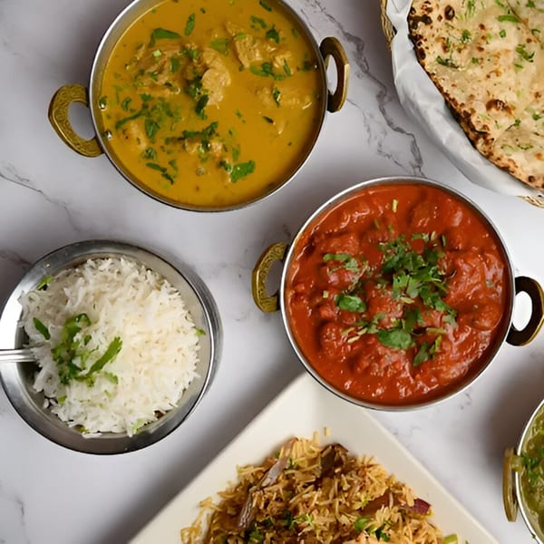 Overhead view of various Indian dishes including curries, rice, and naan bread on a marble surface.